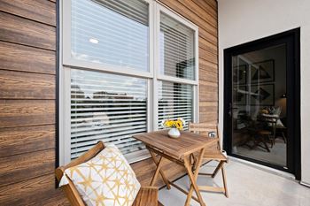 A wooden chair with a cushion is placed in front of a window with blinds.